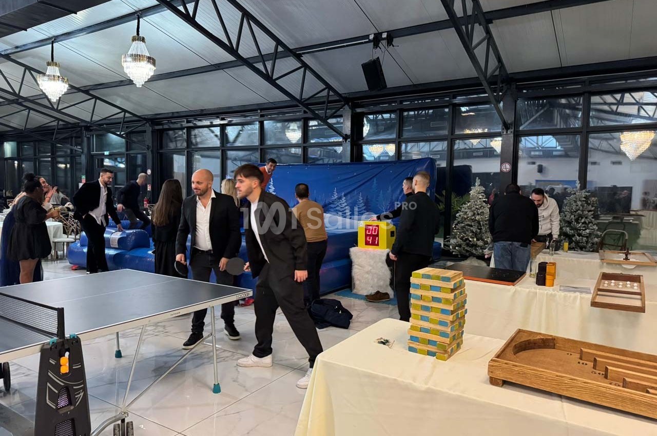 Des personnes jouent et discutent autour de jeux de société et d'une table de ping-pong dans une salle lumineuse.