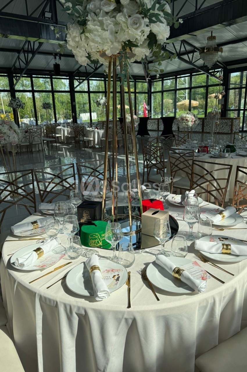 Table ronde élégamment dressée avec nappes blanches, vaisselle raffinée et centre de table floral dans une salle lumineuse.
