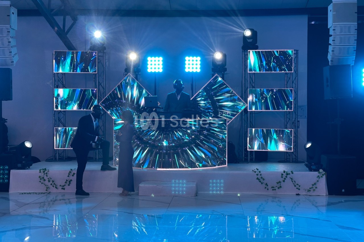 Un DJ mixe sur une scène illuminée avec des écrans LED colorés, devant un couple dansant sur une piste brillante.