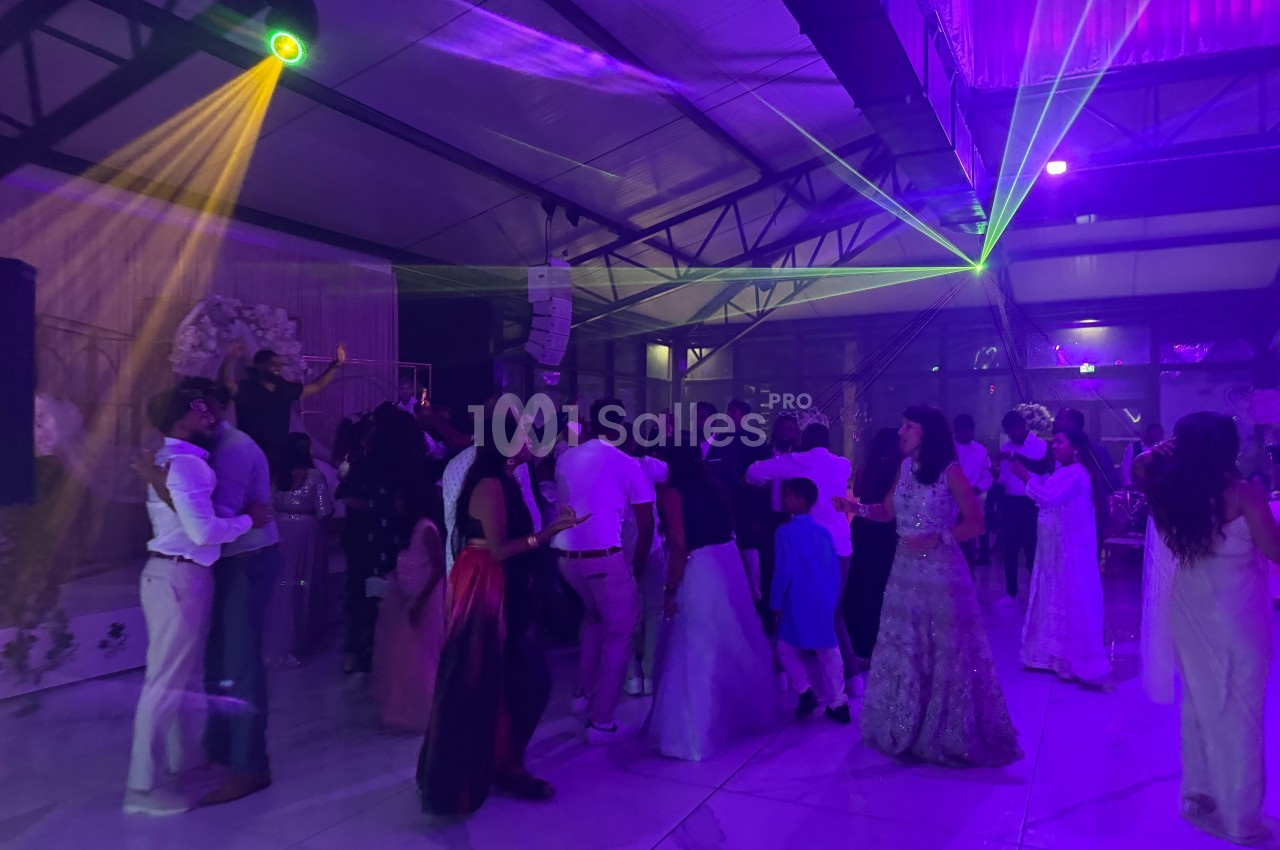 Des personnes dansent sous des jeux de lumières colorées dans une salle de réception spacieuse.
