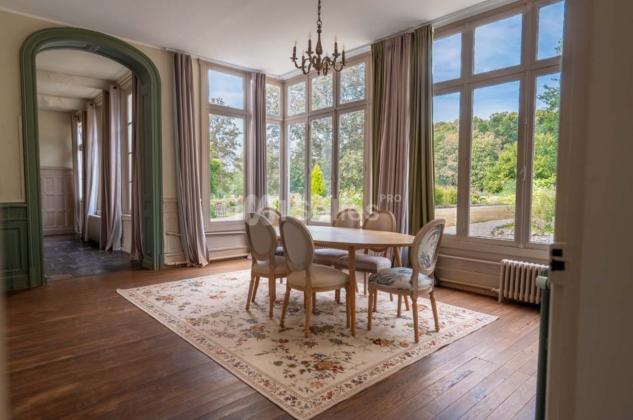 Salle à manger lumineuse avec table ronde, chaises élégantes, grandes fenêtres donnant sur un jardin verdoyant.