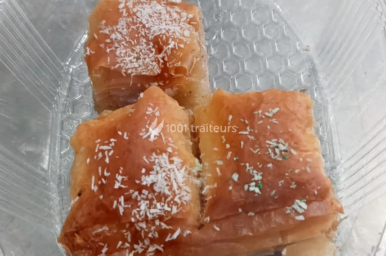 Trois parts de pâtisserie feuilletée dorée, saupoudrées de noix de coco râpée, dans un contenant transparent.