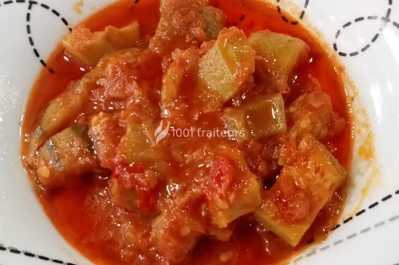 Plat de légumes mijotés dans une sauce tomate rouge, servi dans une assiette blanche avec motifs noirs.