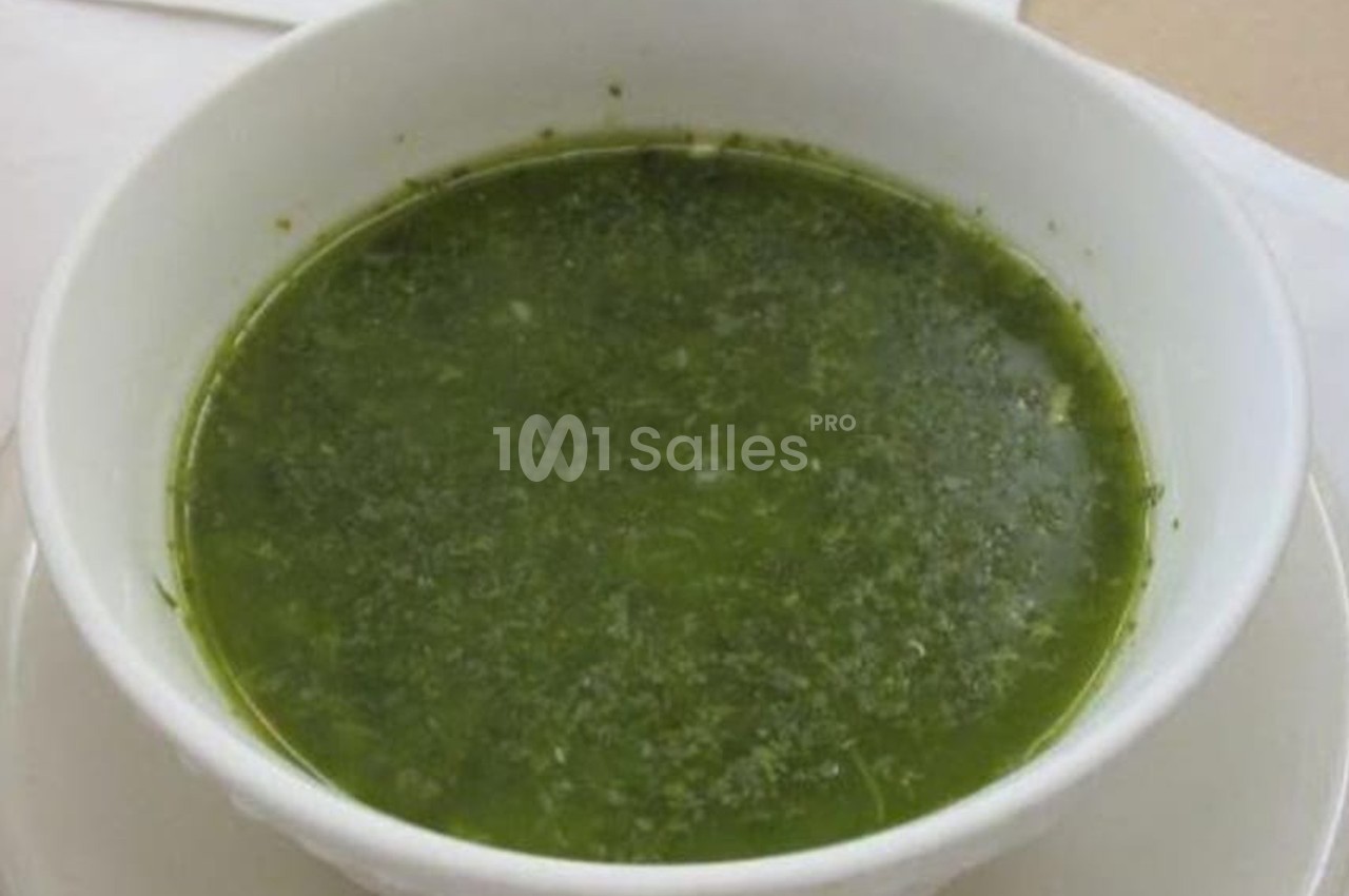 Bol de soupe verte servi dans une assiette blanche sur une table.