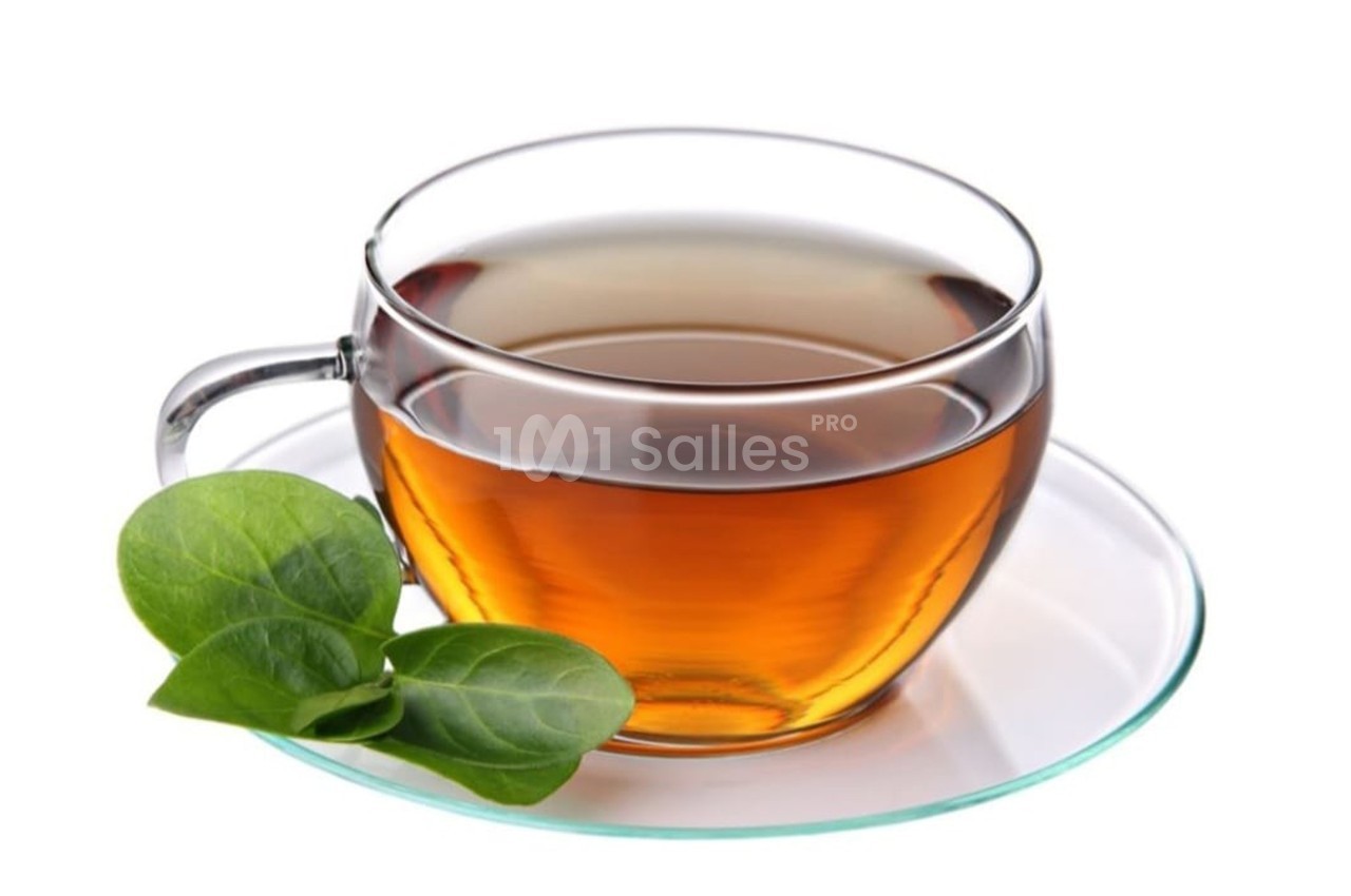 Tasse de thé ambré sur une soucoupe en verre, accompagnée de deux feuilles vertes.
