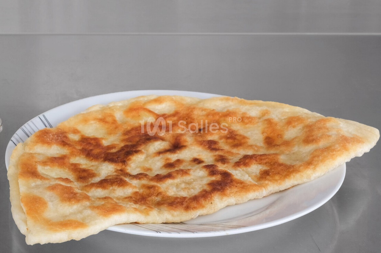 Galette dorée et croustillante servie sur une assiette blanche posée sur une surface métallique.