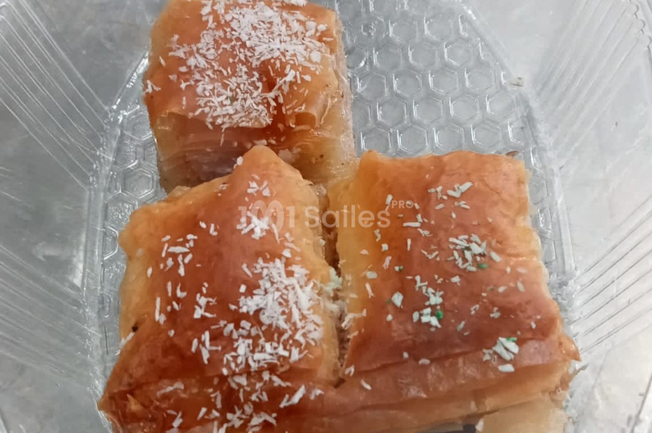 Trois parts de pâtisserie feuilletée dorée, saupoudrées de noix de coco râpée, dans un contenant transparent.