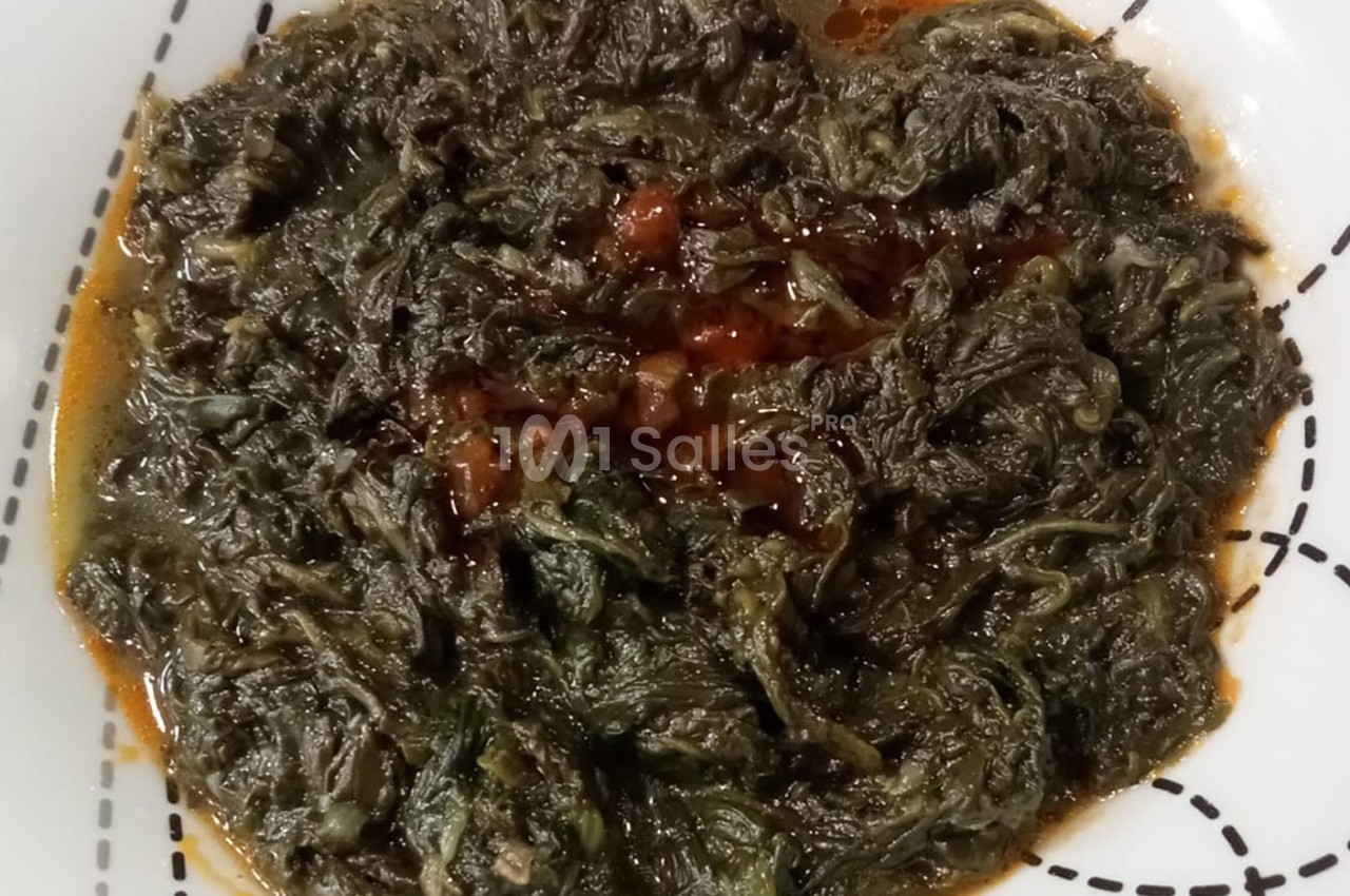 Plat de feuilles de légumes mijotées dans une sauce épicée, présenté dans une assiette blanche.