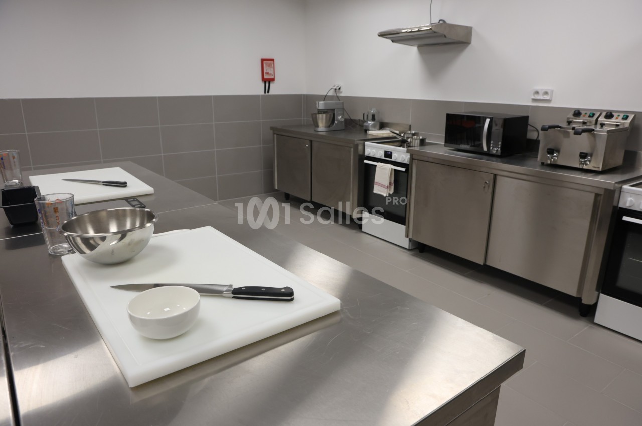 Plan de travail en cuisine professionnelle avec ustensiles, planches à découper et équipements en inox en arrière-plan.