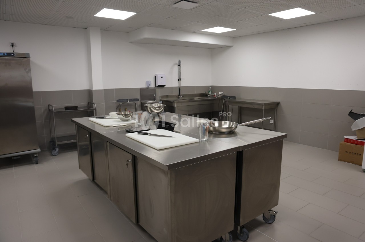 Cuisine professionnelle avec plan de travail en inox, évier, ustensiles et équipements de préparation.