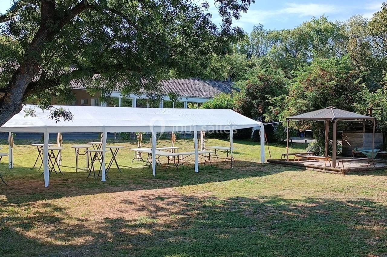 Tentes blanches installées sur une pelouse avec des tables et un puits couvert à proximité, entourés de végétation.