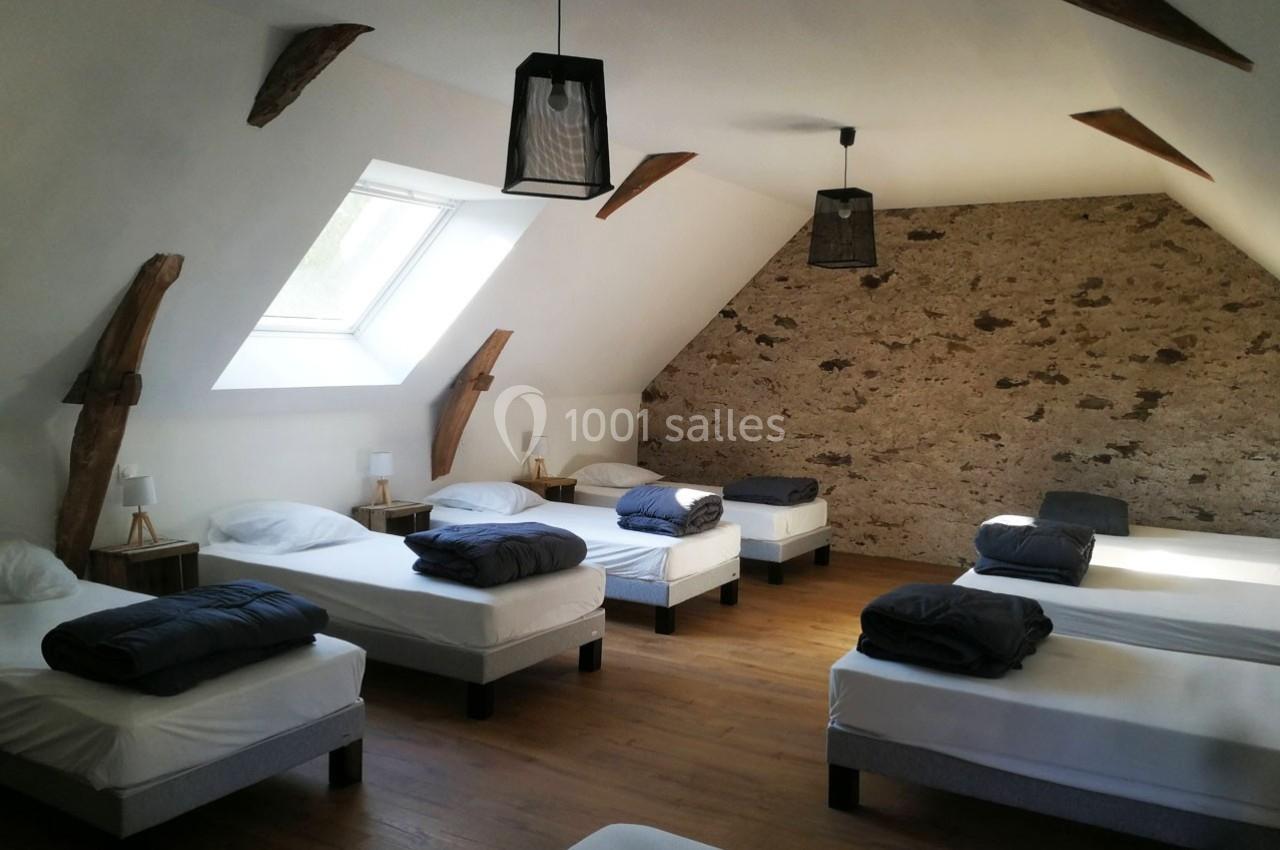 Dortoir lumineux avec six lits simples, murs en pierre apparente, poutres en bois et parquet au sol.