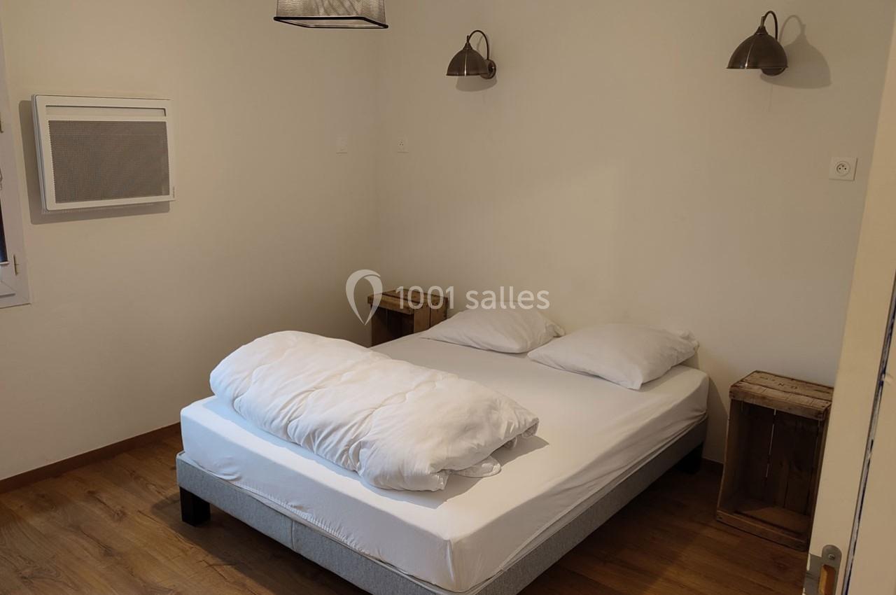 Lit double avec draps blancs dans une chambre minimaliste, parquet au sol et tables de chevet en bois brut.
