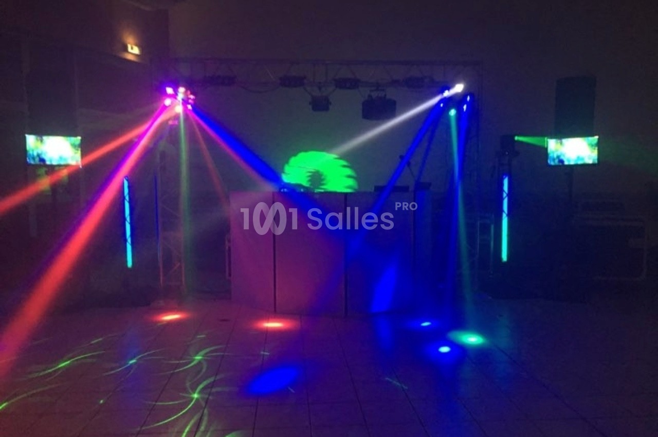 Jeu de lumières colorées projetées dans une salle sombre avec des écrans et un équipement de sonorisation.