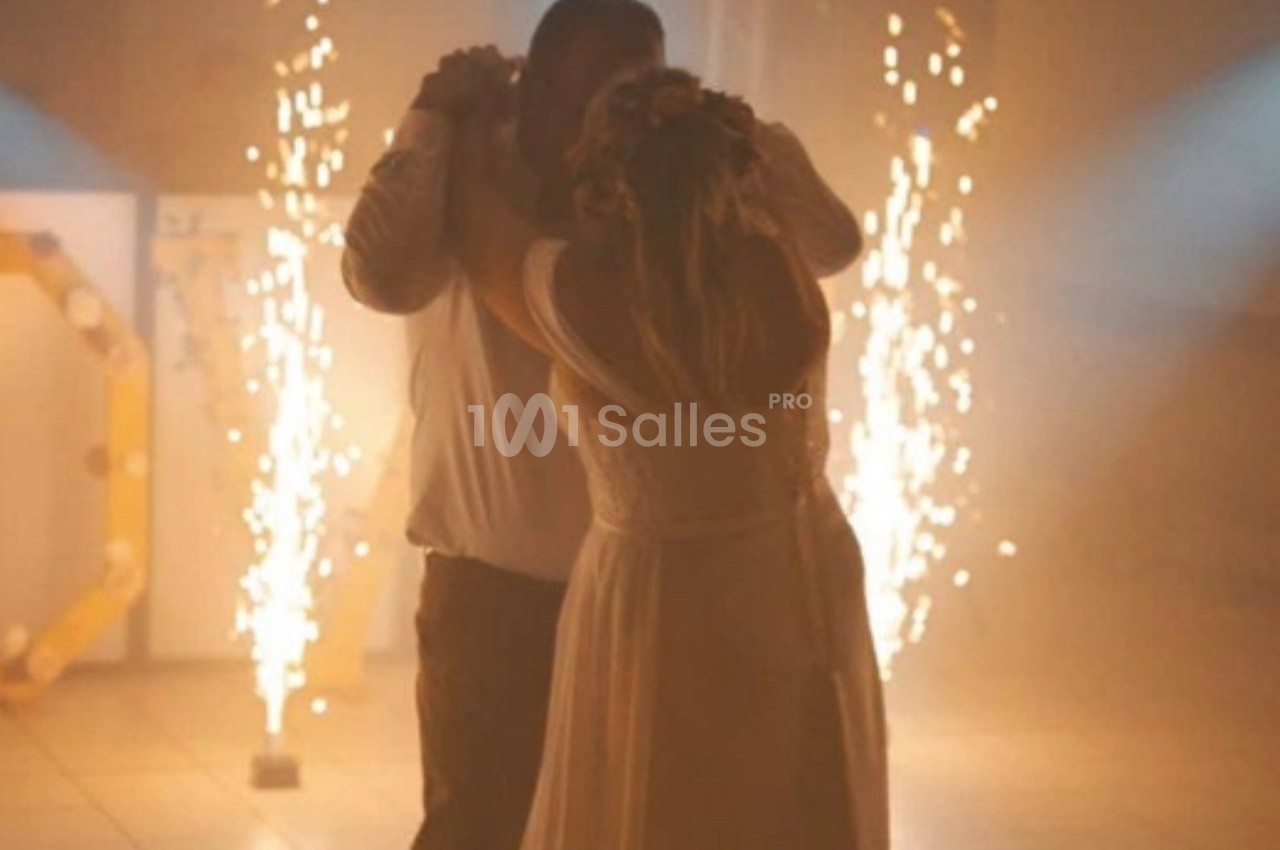 Un couple danse sous des lumières tamisées avec des étincelles en arrière-plan dans une ambiance festive.