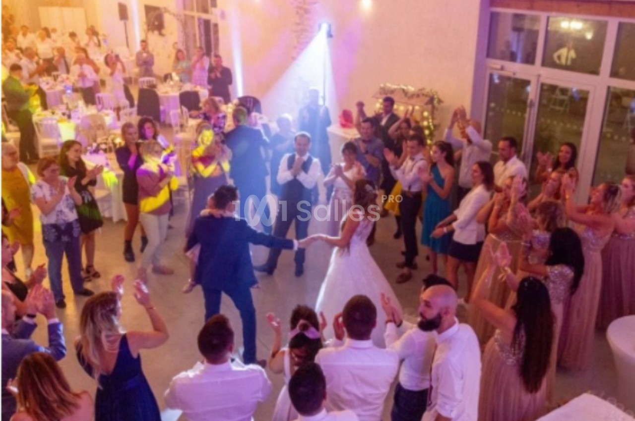 Un couple de mariés danse au centre d'une salle entouré d'invités applaudissant lors d'une réception festive.
