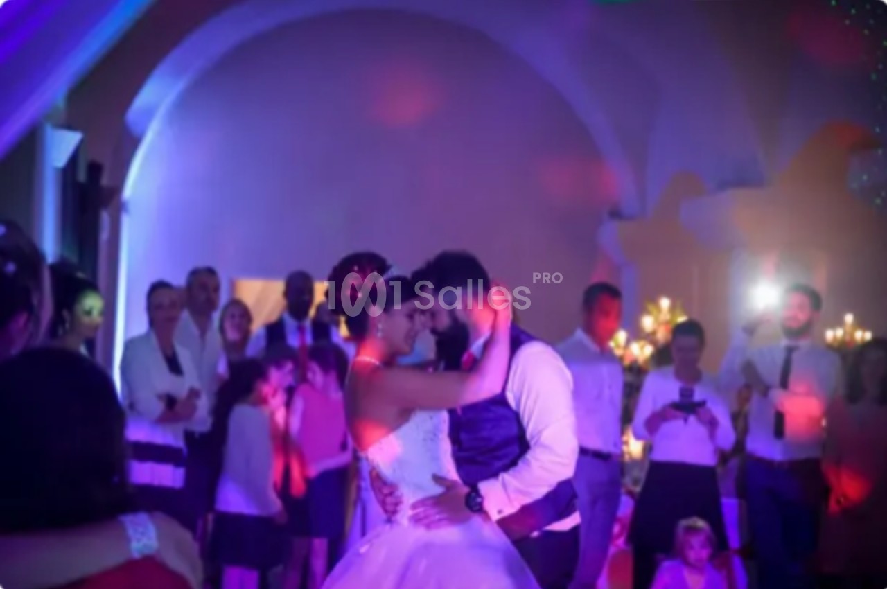 Un couple danse lors de leur mariage, entouré d'invités sous des lumières colorées dans une salle festive.
