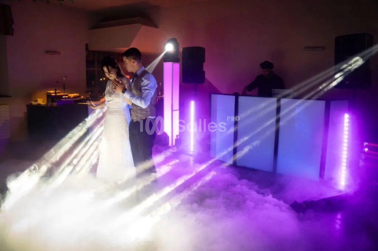 Un couple danse dans une ambiance festive avec éclairages colorés et fumée, un DJ en arrière-plan.