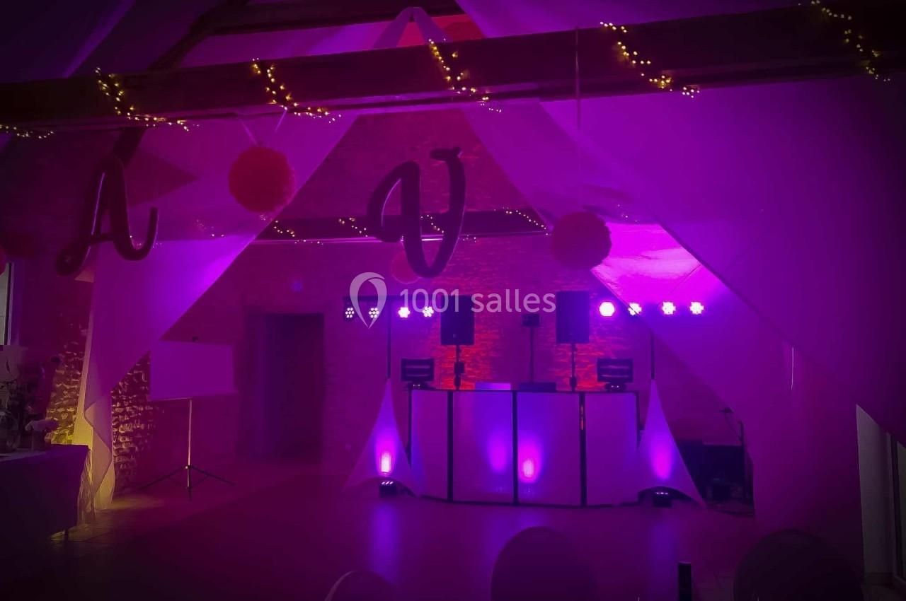 Salle de réception décorée avec des lumières violettes, guirlandes lumineuses et une piste de danse équipée de matériel DJ.