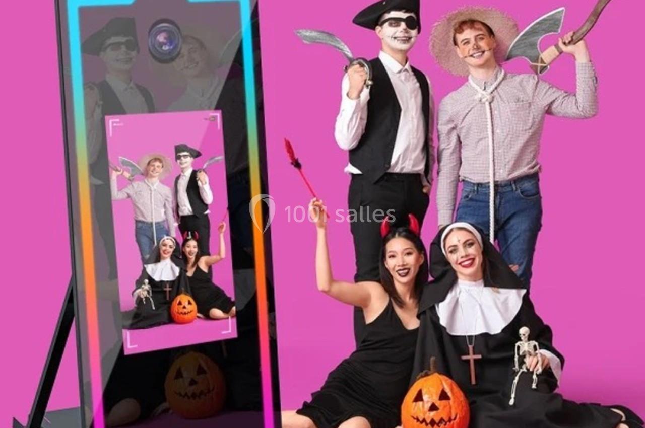 Quatre personnes déguisées pour Halloween posent devant un miroir interactif, avec des citrouilles décoratives au sol.
