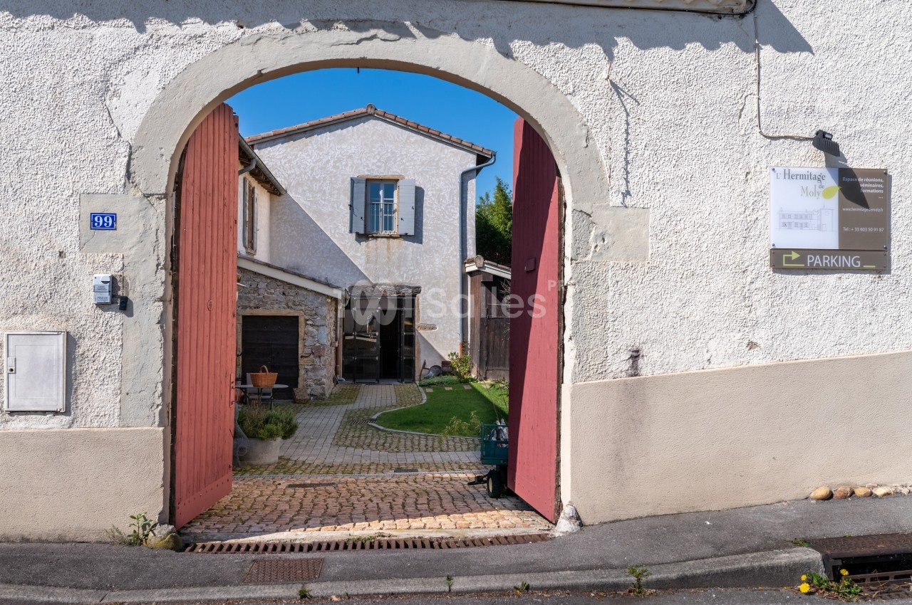 Entrée d'une cour pavée avec un bâtiment en pierre et un panneau indiquant un parking sur le mur.