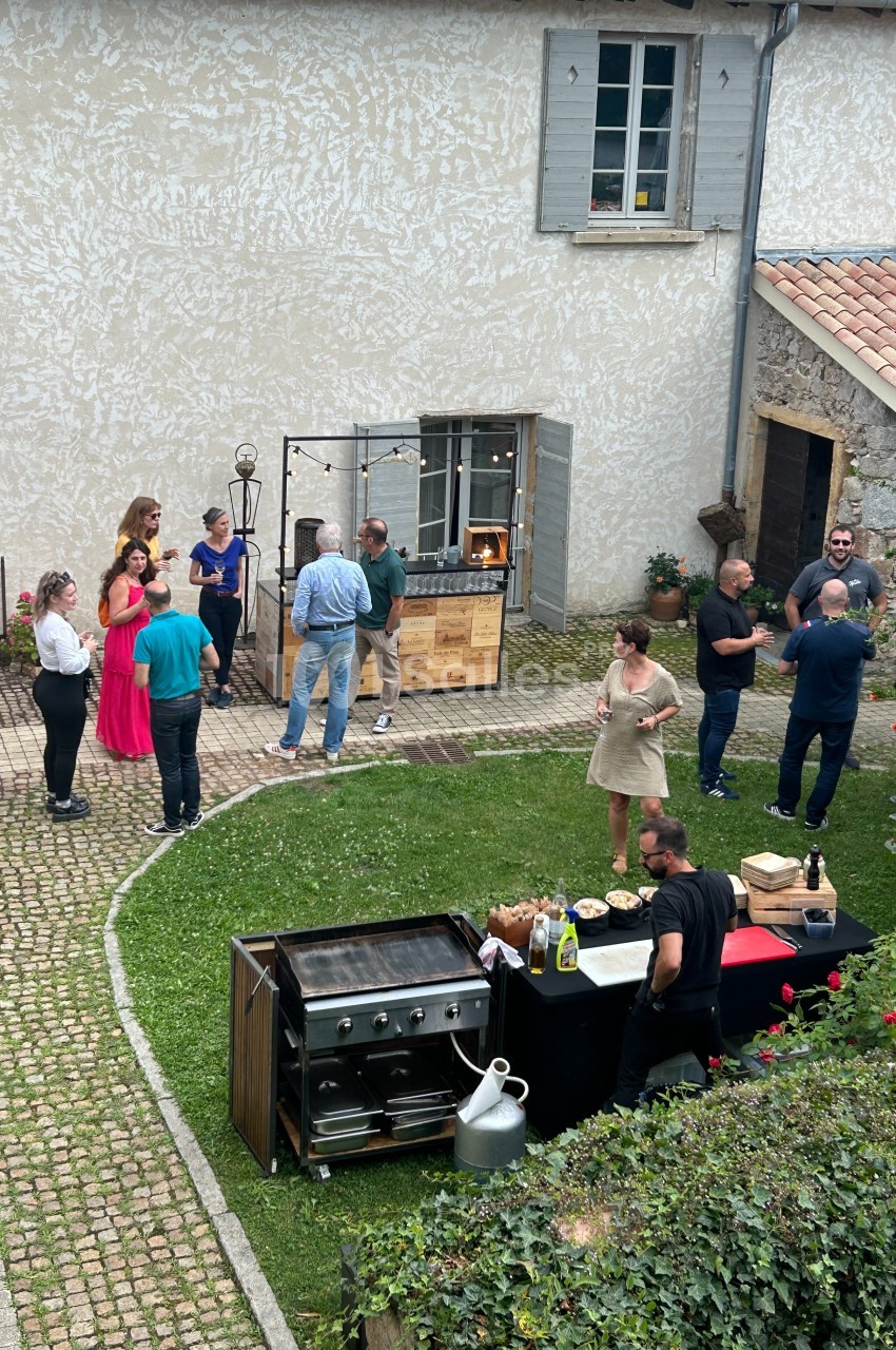 Personnes rassemblées dans une cour pavée avec un barbecue et une table de buffet en premier plan.