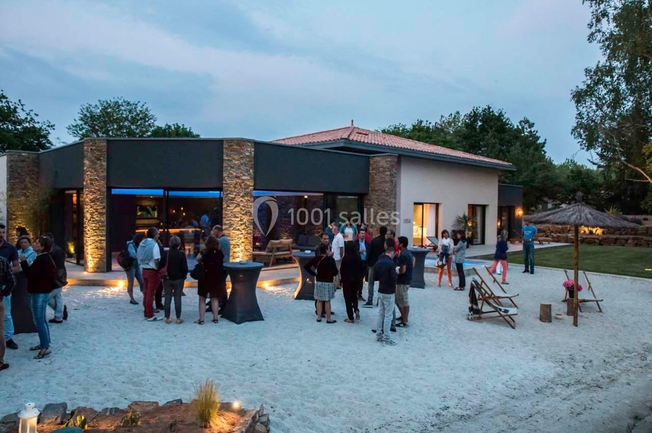 Groupe de personnes rassemblées en soirée devant un bâtiment moderne avec éclairage extérieur et espace aménagé.