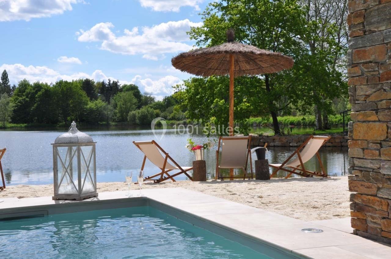 Chaises longues et parasol en bord de lac, avec une piscine au premier plan et un ciel dégagé en arrière-plan.