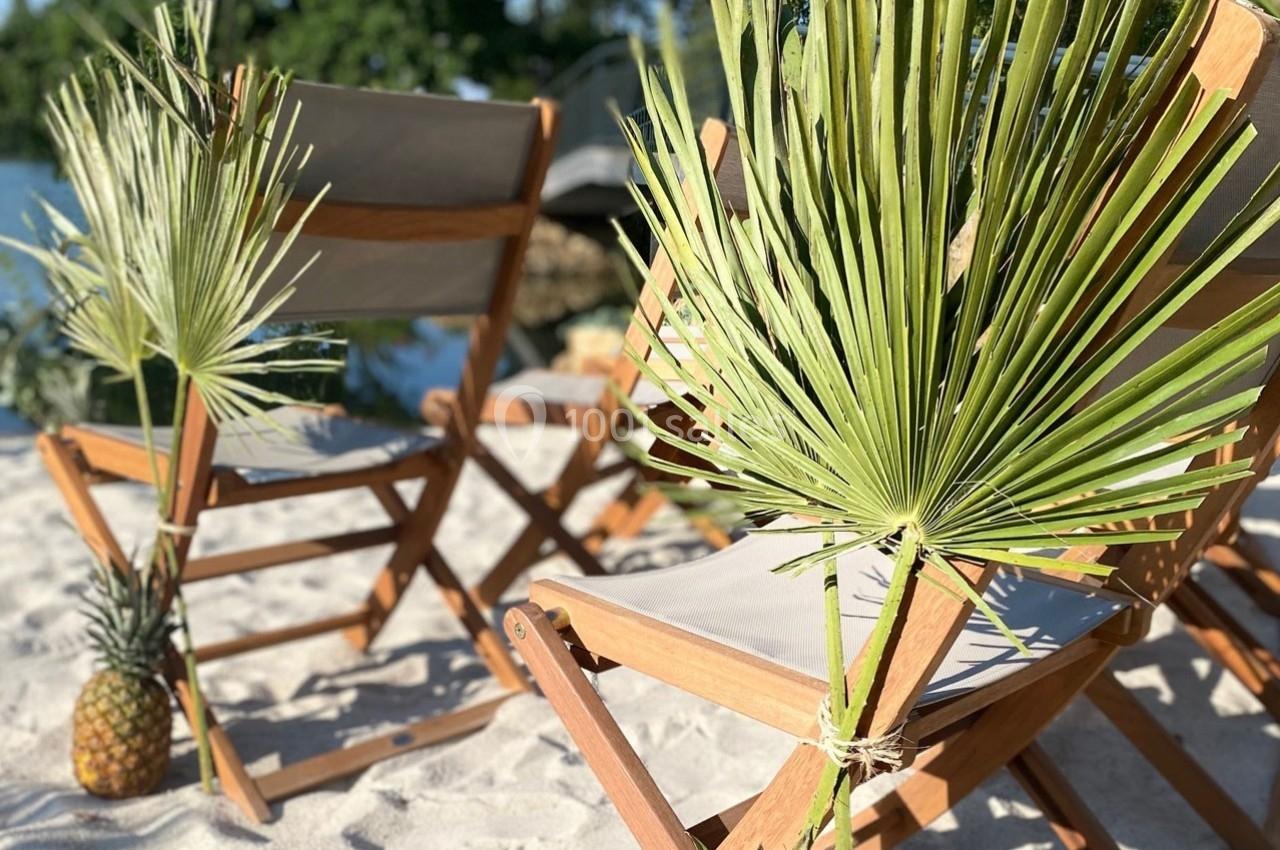 Chaises pliantes en bois avec des feuilles de palmier décoratives, disposées sur une plage ensoleillée.