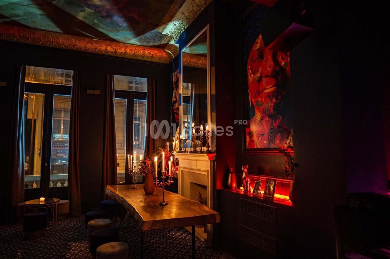 Salle tamisée avec une table en bois, chandeliers allumés, miroirs, et décorations murales colorées.