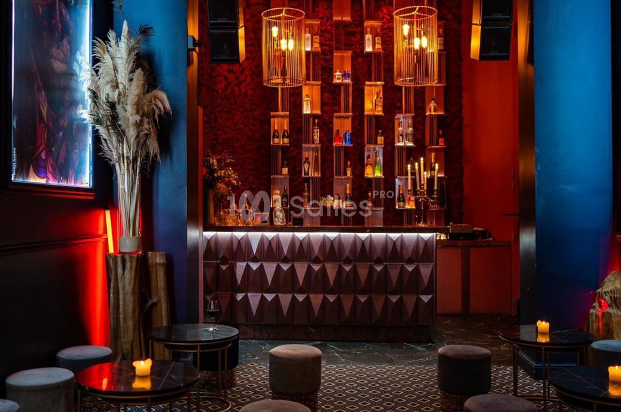 Bar élégant avec comptoir géométrique, étagères illuminées de bouteilles, tabourets bas et ambiance tamisée.