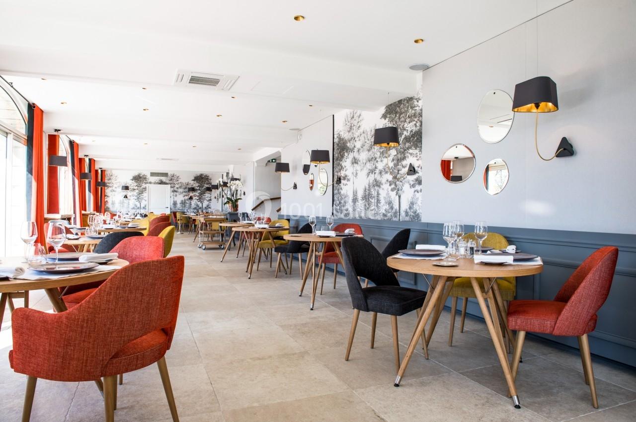 Salle de restaurant lumineuse avec des tables dressées, des chaises colorées et une décoration murale moderne.