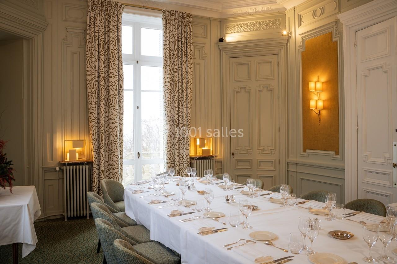 Salle à manger élégante avec une grande table dressée, entourée de chaises, éclairée par des appliques murales et une…