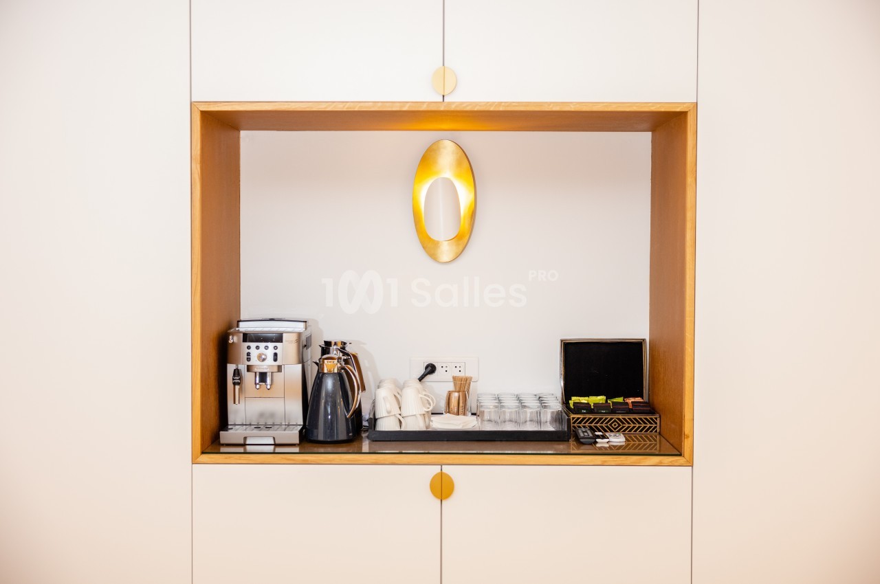 Espace kitchenette avec machine à café, bouilloire, tasses, verres et accessoires disposés sur une étagère encastrée.