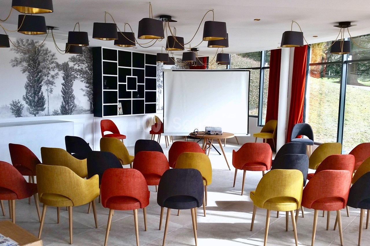 Salle lumineuse aménagée avec des chaises colorées disposées face à un écran de projection.