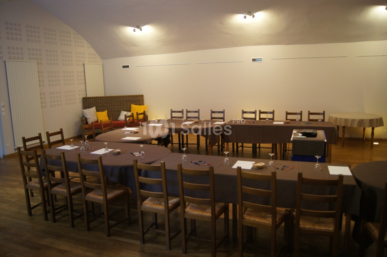 Salle de réunion avec tables disposées en U, chaises en bois, feuilles, stylos et éclairage tamisé.