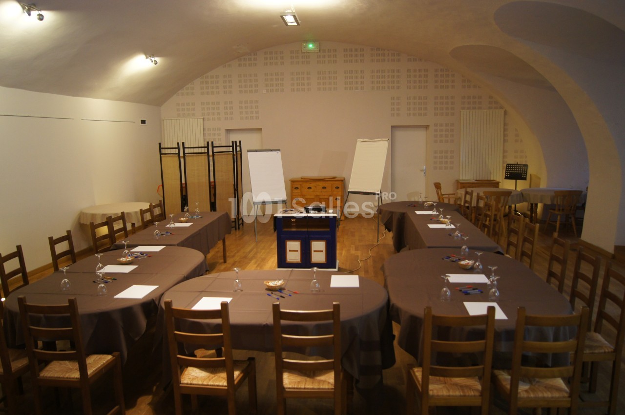 Salle de réunion avec tables disposées en U, chaises en bois, tableaux blancs et éclairage tamisé.