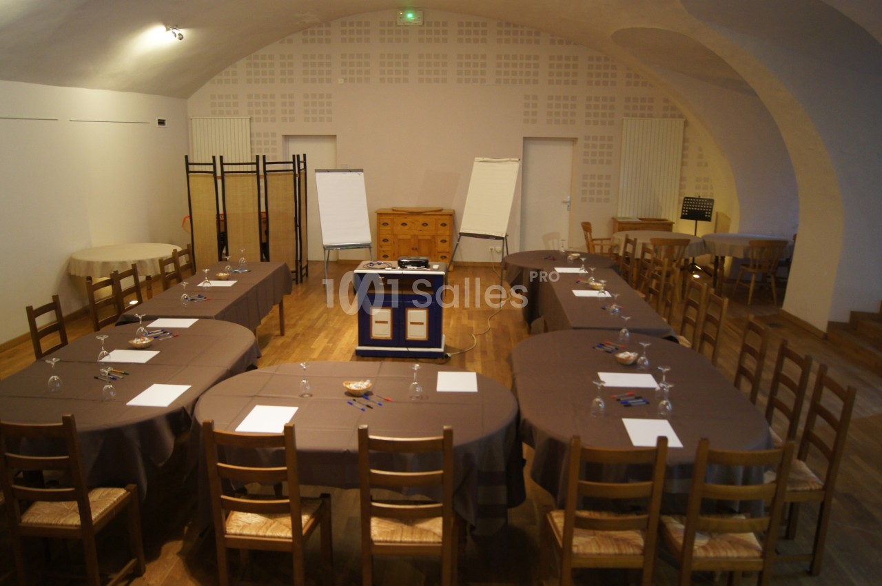 Salle de réunion avec tables disposées en U, chaises en bois, paperboards, et matériel de présentation au centre.