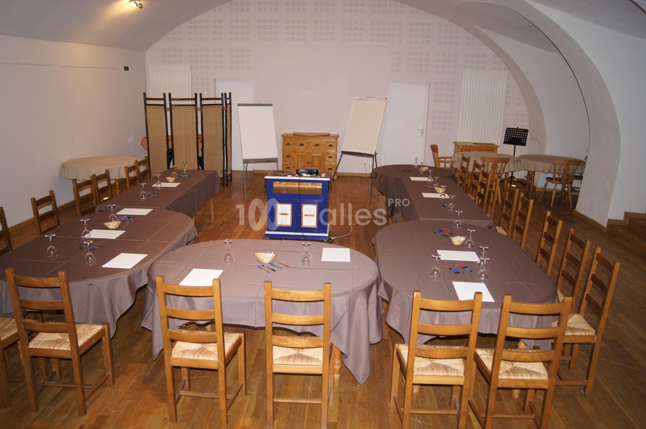 Salle de réunion aménagée en U avec tables, chaises en bois, paperboards et matériel de présentation.