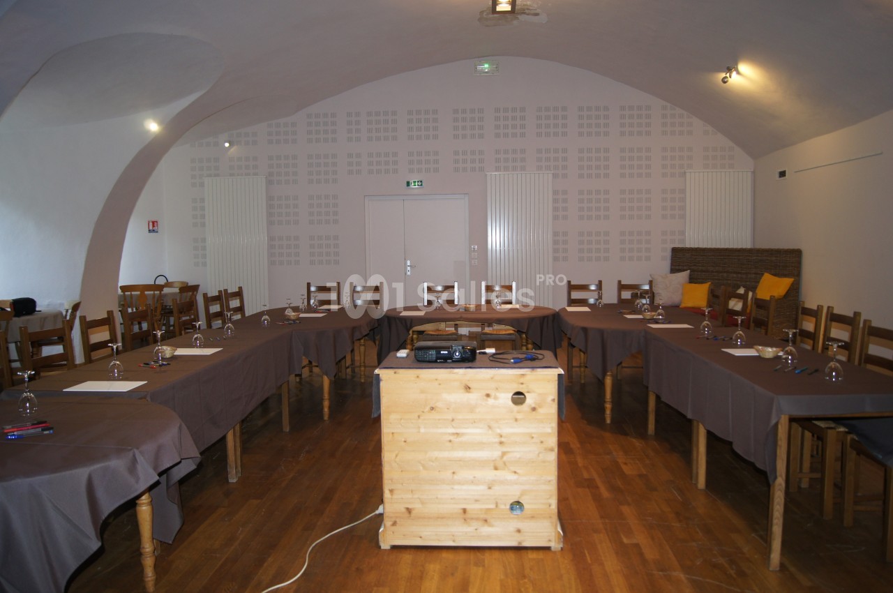 Salle de réunion avec tables disposées en U, nappes brunes, chaises en bois et projecteur sur une table centrale.