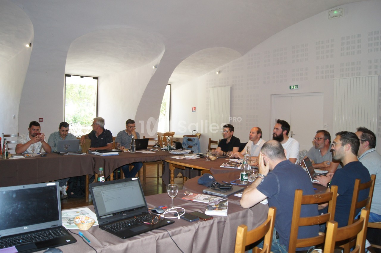 Un groupe de personnes assises autour de tables en réunion dans une salle lumineuse avec des ordinateurs portables.