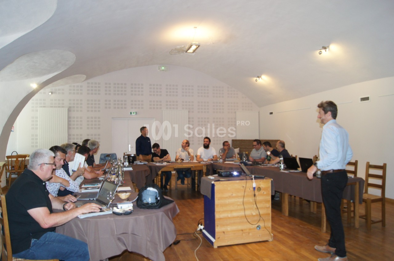 Un groupe de personnes assises autour de tables en réunion dans une salle avec un plafond voûté.