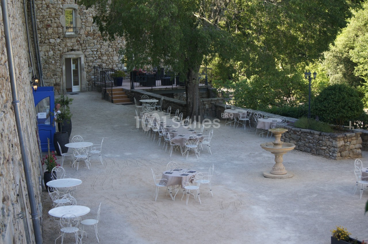 Cour extérieure avec tables et chaises en fer forgé, entourée de verdure et d'un bâtiment en pierre.