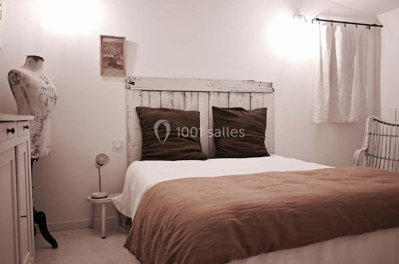 Chambre lumineuse avec un lit double, tête de lit en bois blanc, coussins marron et décoration sobre.