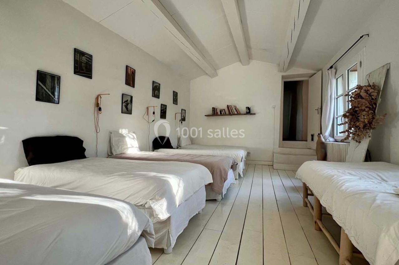Chambre lumineuse avec quatre lits simples alignés, décor minimaliste et murs ornés de cadres.
