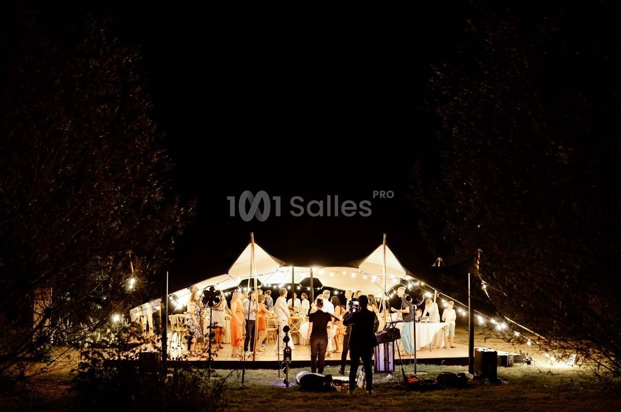 Tente éclairée la nuit accueillant un groupe de personnes lors d'un événement en plein air.