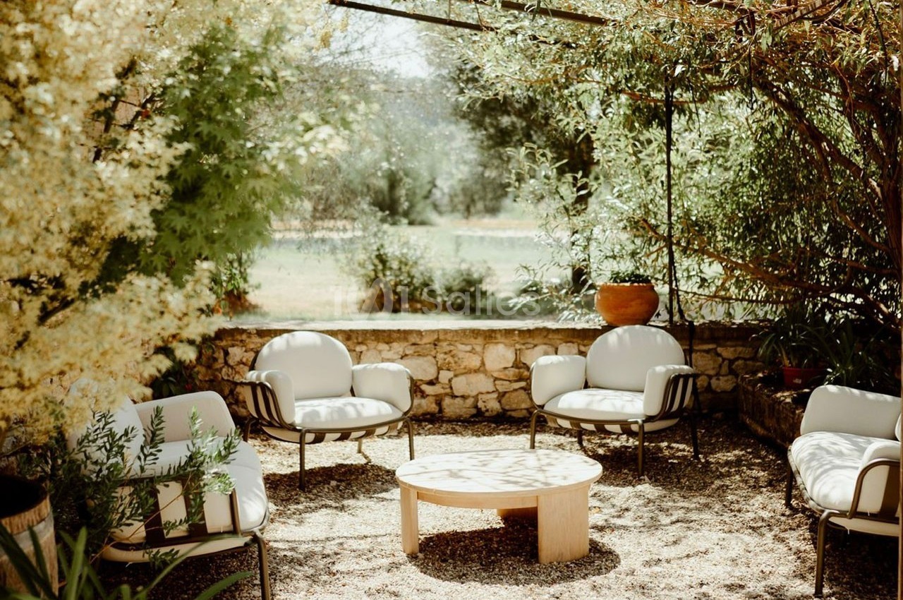 Mobilier de jardin avec quatre fauteuils et une table basse, disposés sous une pergola ombragée entourée de verdure.