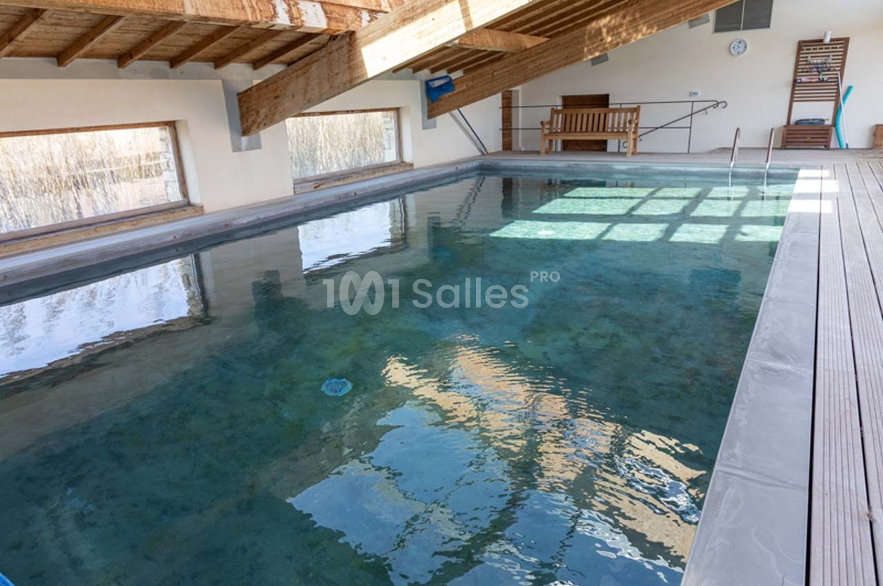 Piscine intérieure avec eau claire, entourée de murs clairs, grandes fenêtres et plafond en bois.