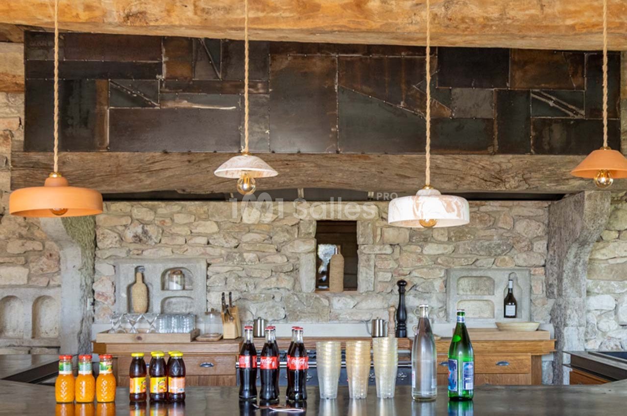 Comptoir de cuisine rustique avec boissons variées, lampes suspendues et mur en pierre apparente.