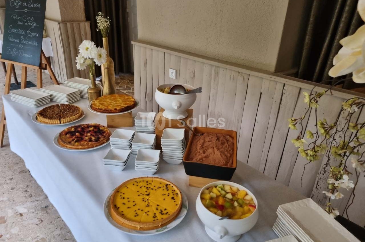 Buffet de desserts avec tartes, mousse au chocolat, salade de fruits et piles d'assiettes blanches.